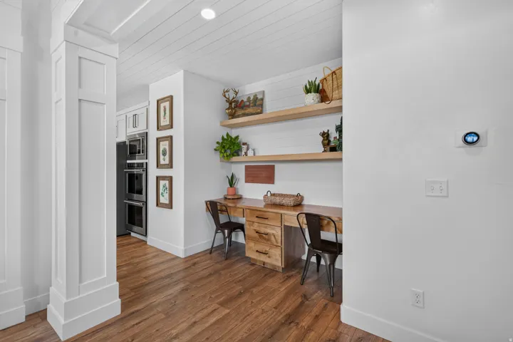Wood-finish flooring, built-in wooden desks with drawers, wall-mounted wooden shelving, and a shiplap ceiling treatment