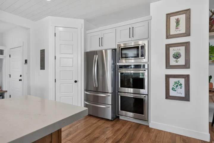 White shaker-style cabinetry with stainless steel appliances, wood-finish flooring, and a light-toned countertop