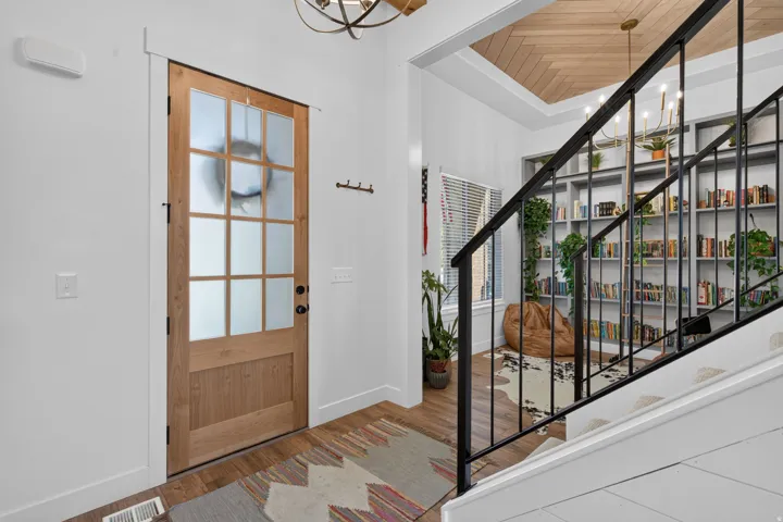 Wood-finish flooring, staircase with metal railing, built-in shelving, glass-paned entry door, and wood-paneled ceiling