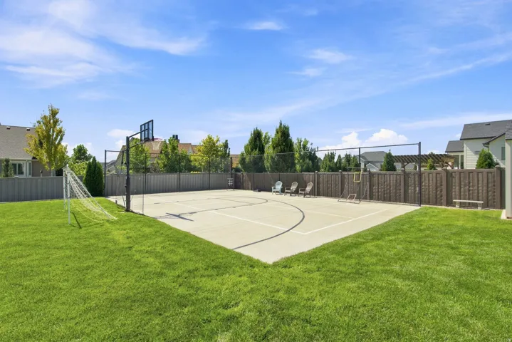 Expansive green lawn with a dedicated sports court, featuring a basketball hoop and court markings, enclosed by a privacy fence
