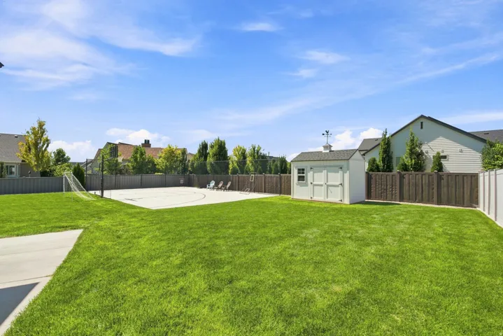 Expansive green lawn with a concrete patio, wood privacy fencing, and a dedicated concrete sports court