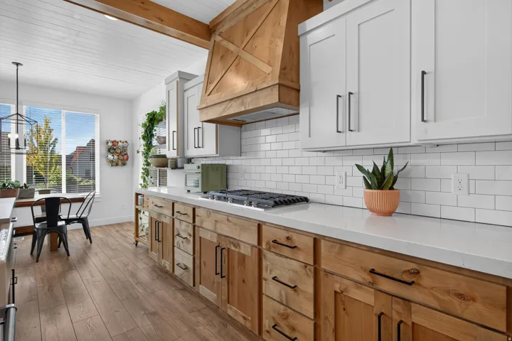 White shaker-style upper cabinetry, natural wood-finish lower cabinetry, light-toned countertops, subway tile backsplash, and wood-finish flooring