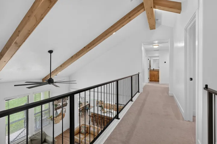 Vaulted ceiling with exposed wood beams, overhead ceiling fan, and black metal railing overlooking the lower level