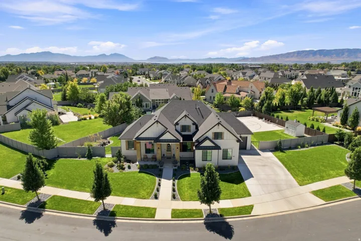 Modern farmhouse exterior with dark trim and a prominent front porch, expansive front lawn with mature trees, concrete driveway with ample parking, fenced backyard with a sport court, and a detached storage shed