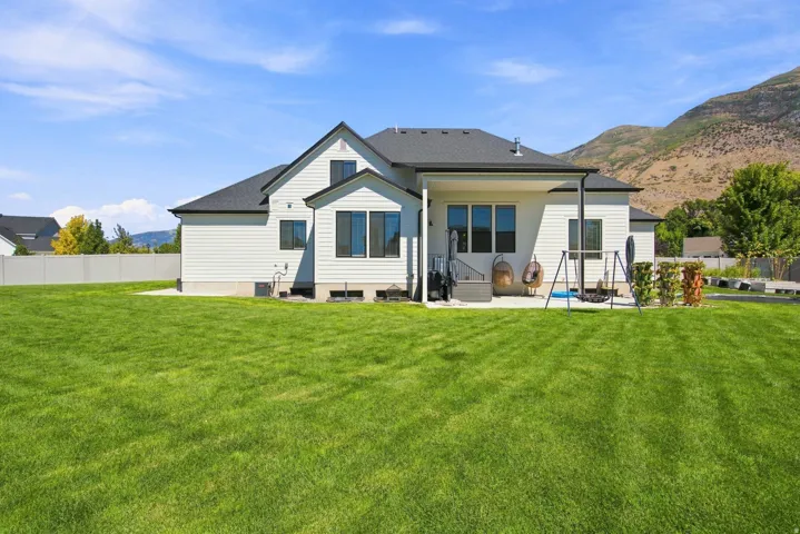 Expansive lawn area with a concrete patio, covered porch, and mountain backdrop