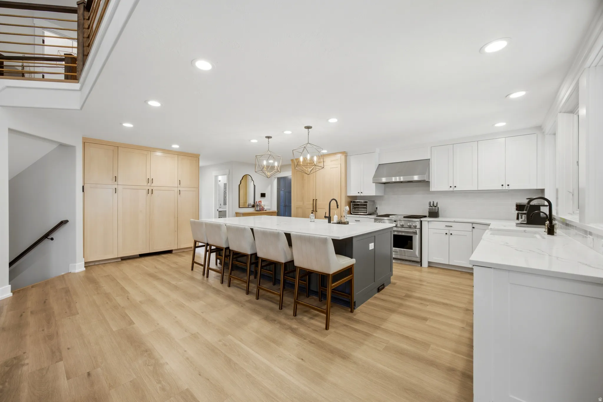 Spacious kitchen featuring white cabinetry, light wood-finish flooring, a large island with seating, stainless steel appliances, and recessed lighting