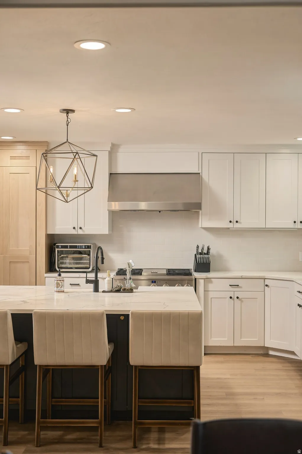 White shaker cabinetry, stainless steel range hood, stone countertops, geometric pendant lighting, and wood-finish flooring