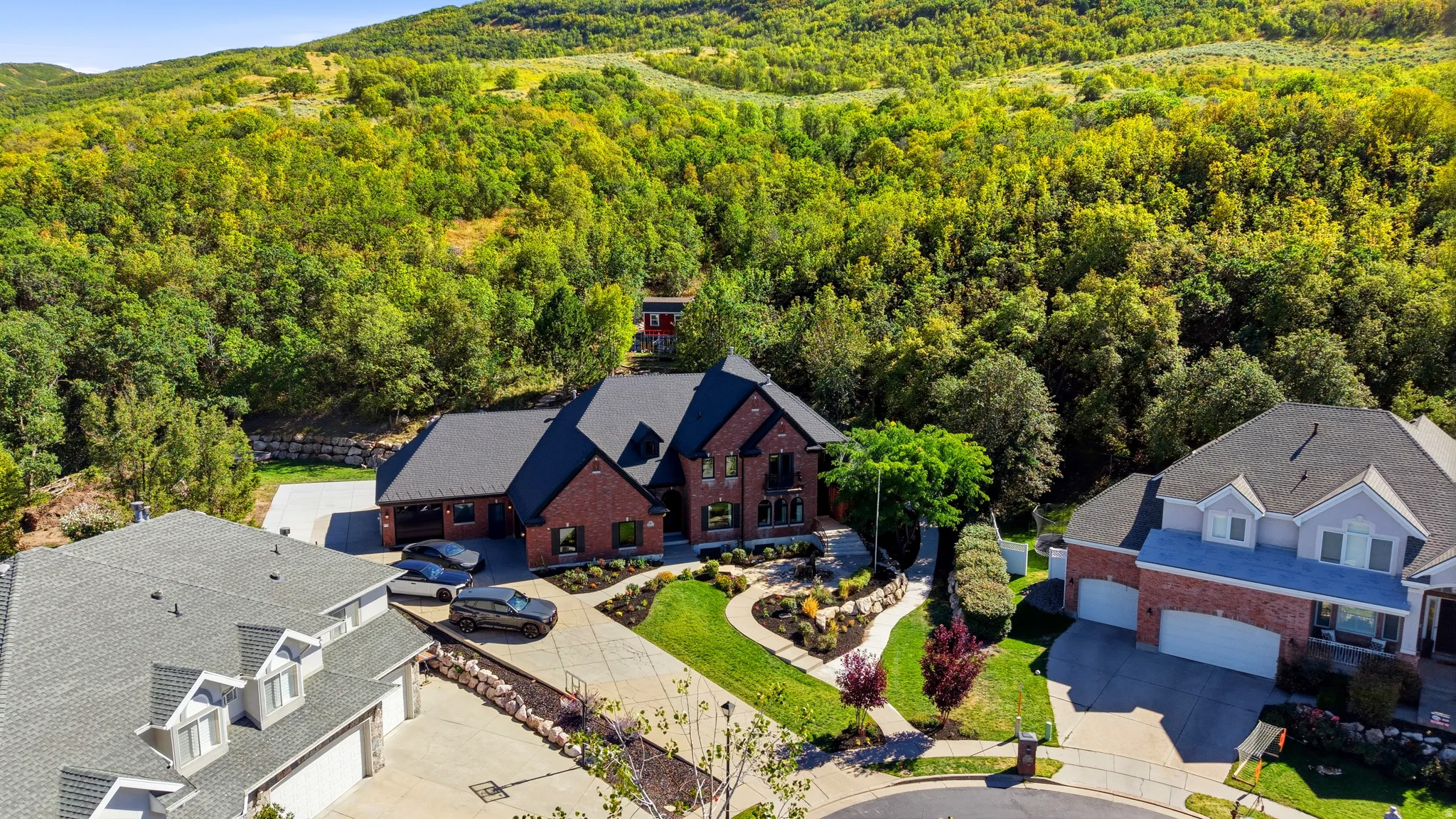 Red brick facade, black shingled roof, manicured landscaping, multi-level design, and concrete driveway
