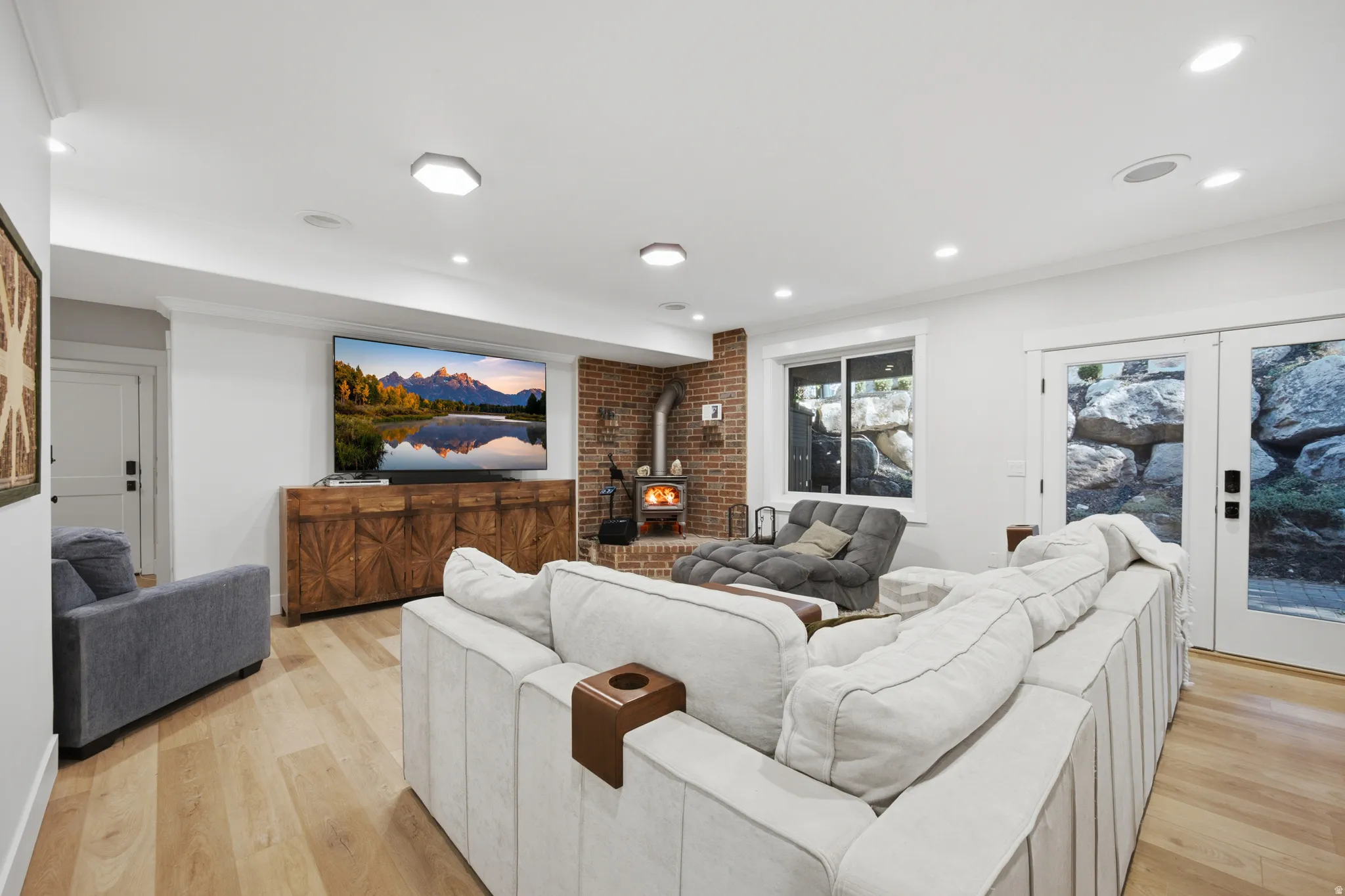 Recessed lighting, wood-finish flooring, exposed brick accent wall, freestanding wood-burning stove, and French doors