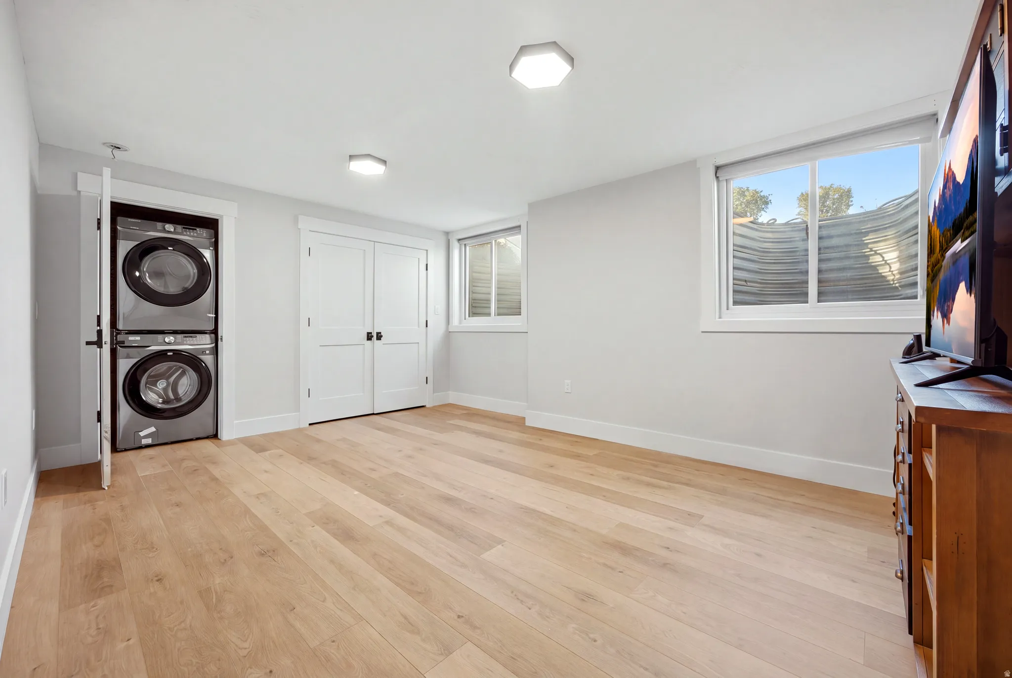 Light wood-finish flooring, recessed lighting, and a stacked washer and dryer unit