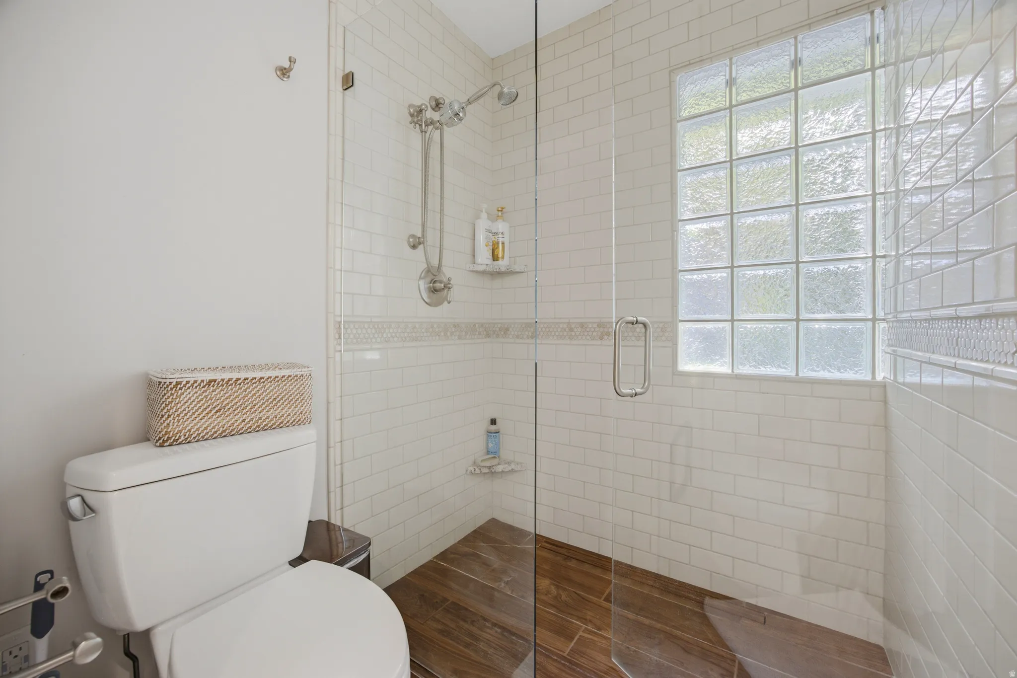 Glass-enclosed shower with subway tile walls, a decorative tile accent, and a glass block window
