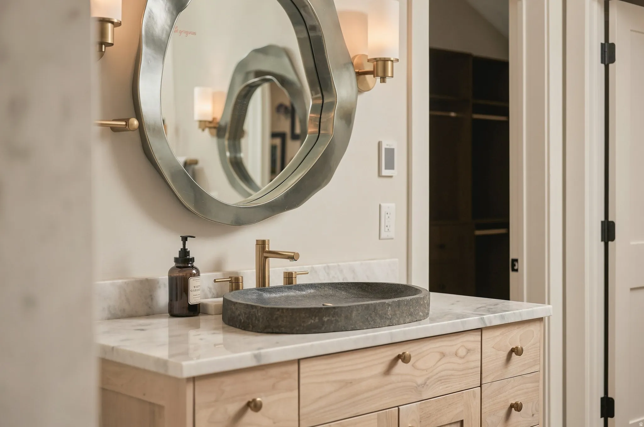 Natural wood vanity with multiple drawers, stone vessel sink, gold-tone faucet, and marble-finish countertop