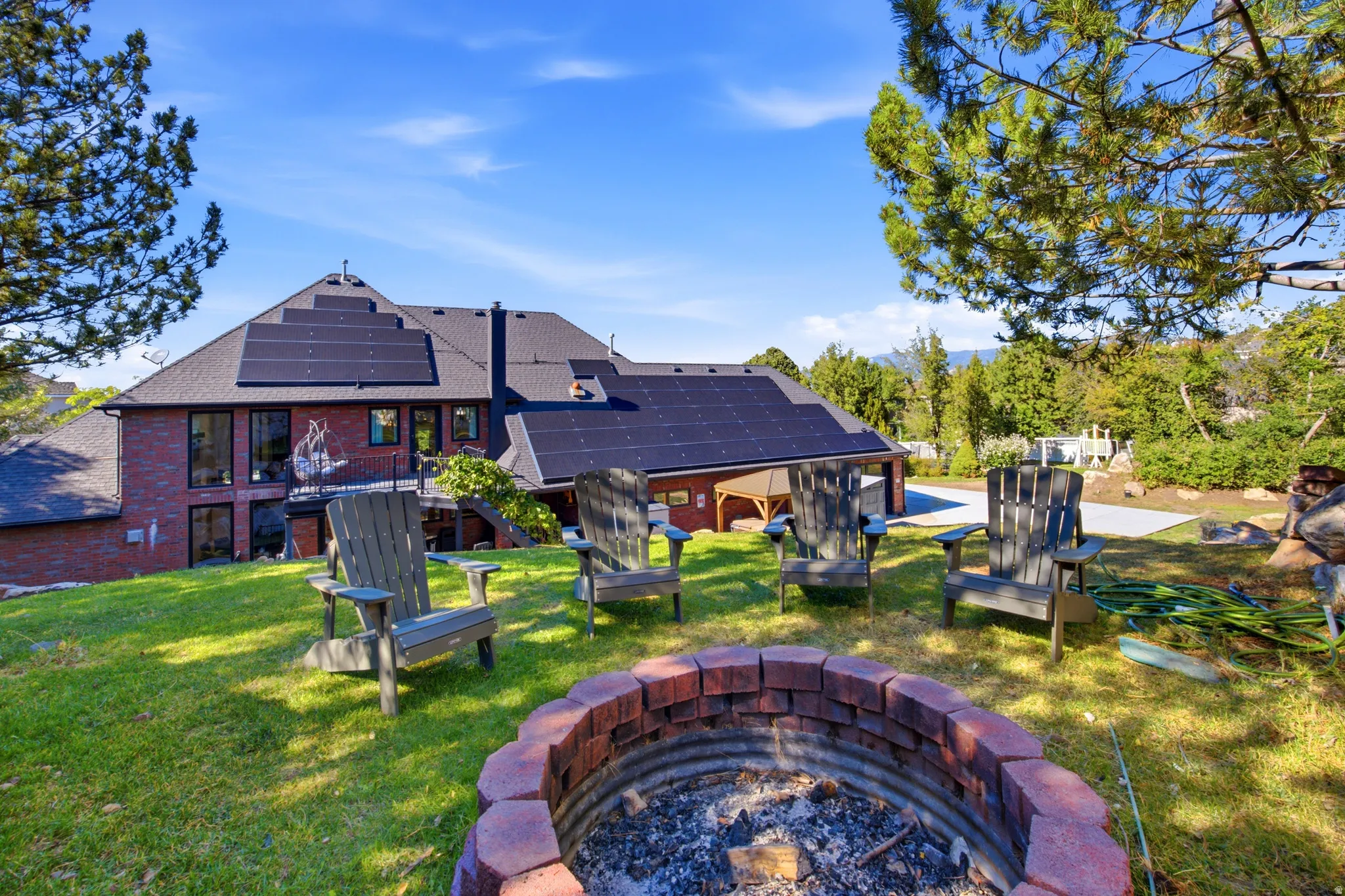Expansive backyard with a brick-lined fire pit, mature trees, and a terraced lawn