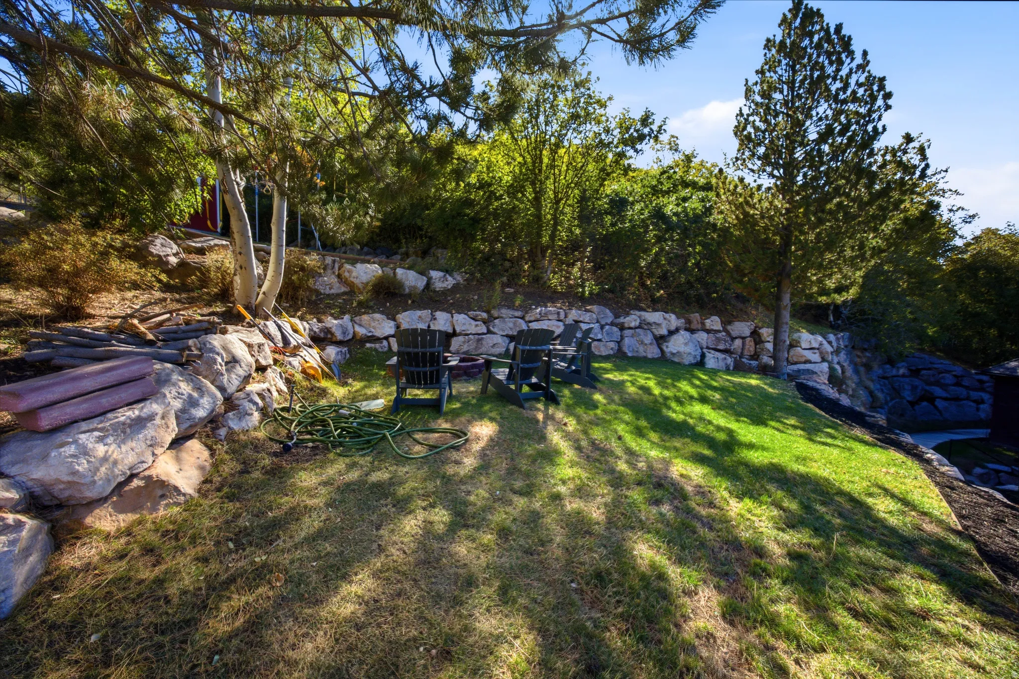 Terraced landscaping with natural stone retaining walls, mature trees, and a grassy area