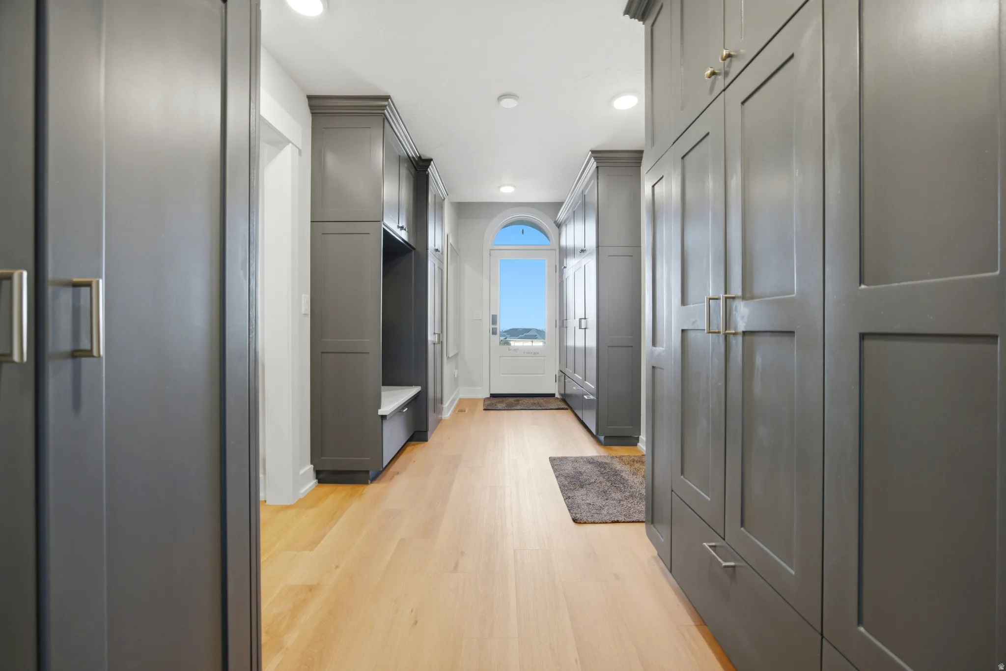 Hallway featuring built-in gray cabinetry, integrated bench seating, and light wood-finish flooring