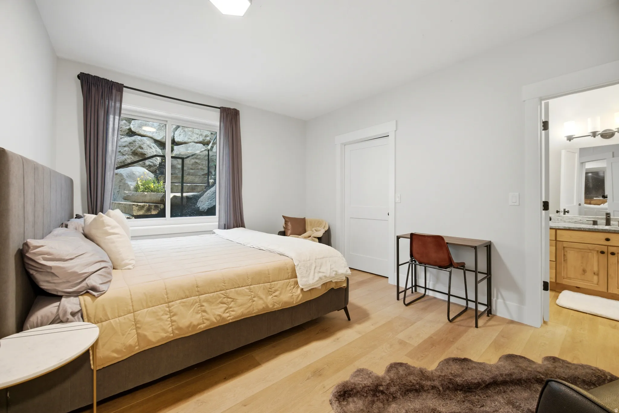 Light-toned wood-finish flooring, white walls, and a window with exterior rock landscaping