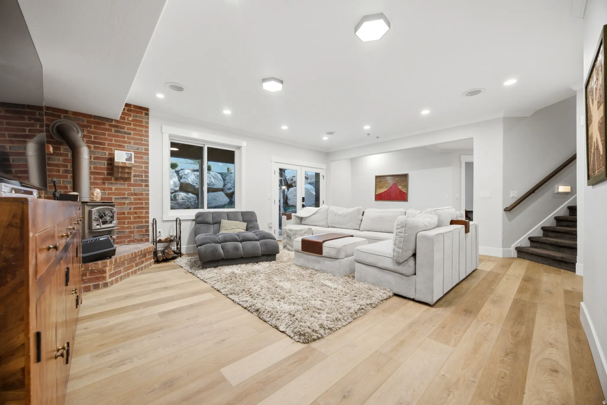 Wood-finish flooring, brick-clad fireplace with a wood stove, recessed lighting, and a staircase with a wood handrail