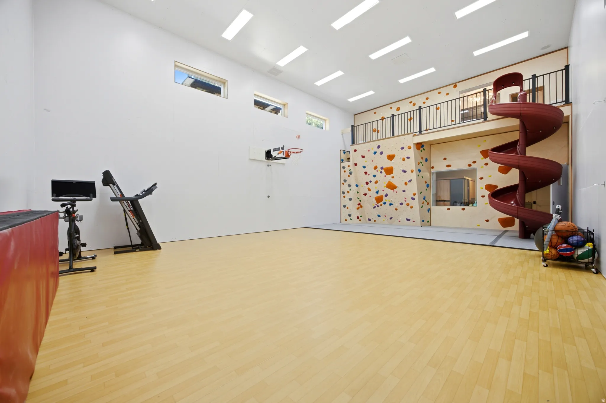 Expansive recreational space featuring wood-finish flooring, a built-in climbing wall, an indoor spiral slide, and a basketball hoop