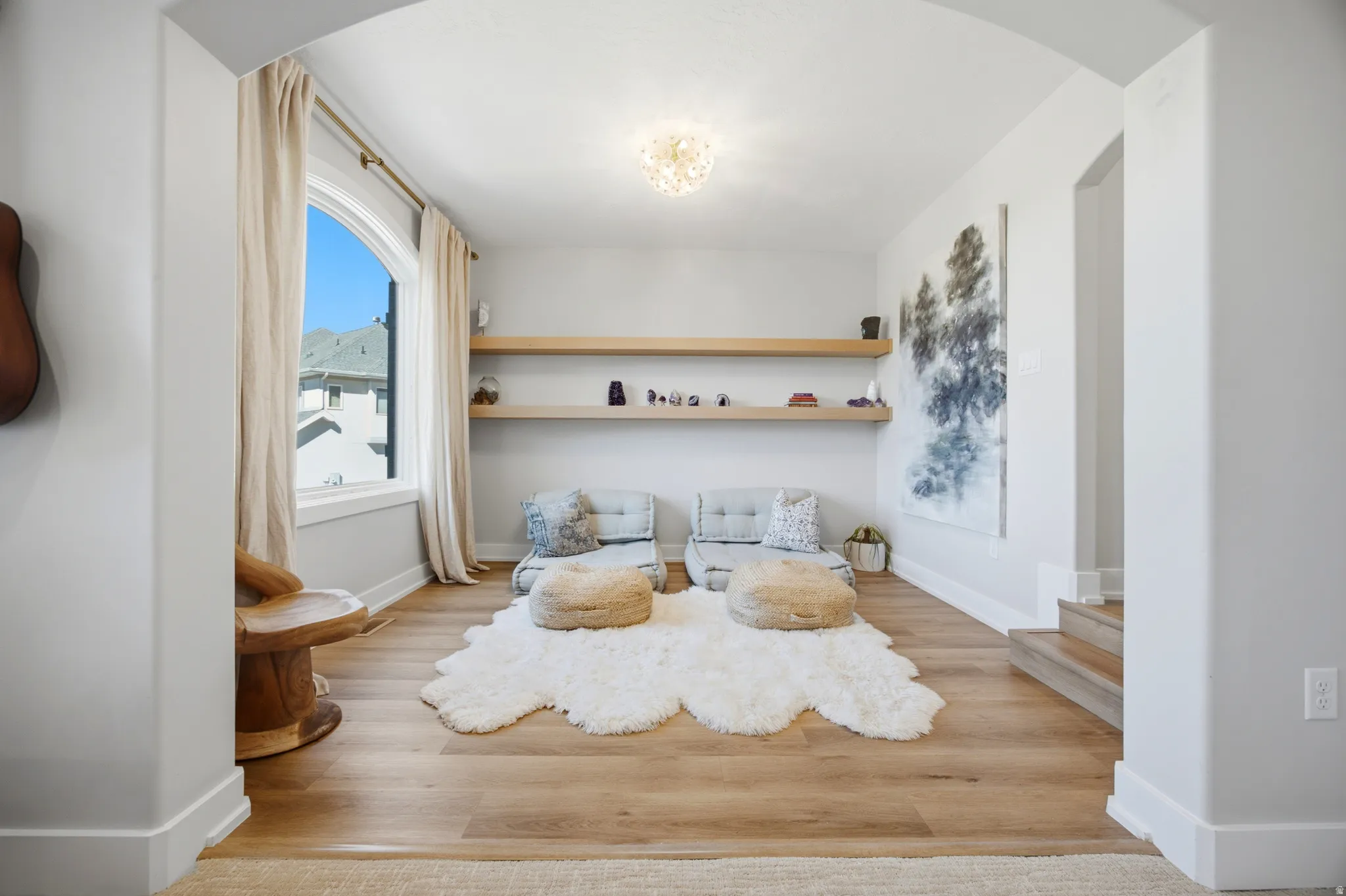 Arched entryway leading to a room with wood-finish flooring, an arched window, and two built-in floating shelves
