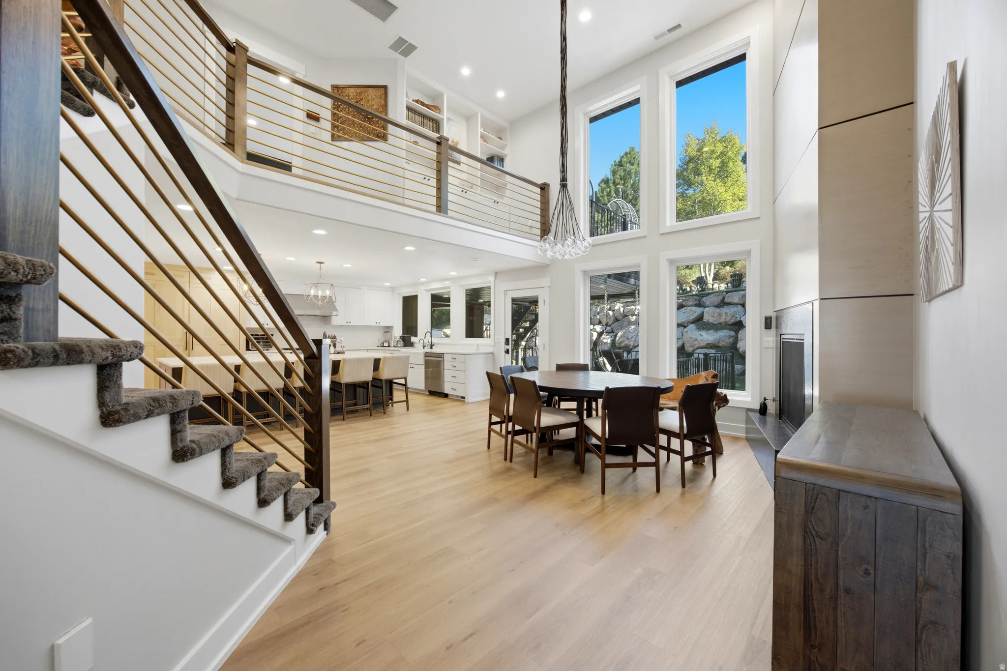 Open-concept living space with light wood-finish flooring, a two-story ceiling, and a prominent staircase with cable railings