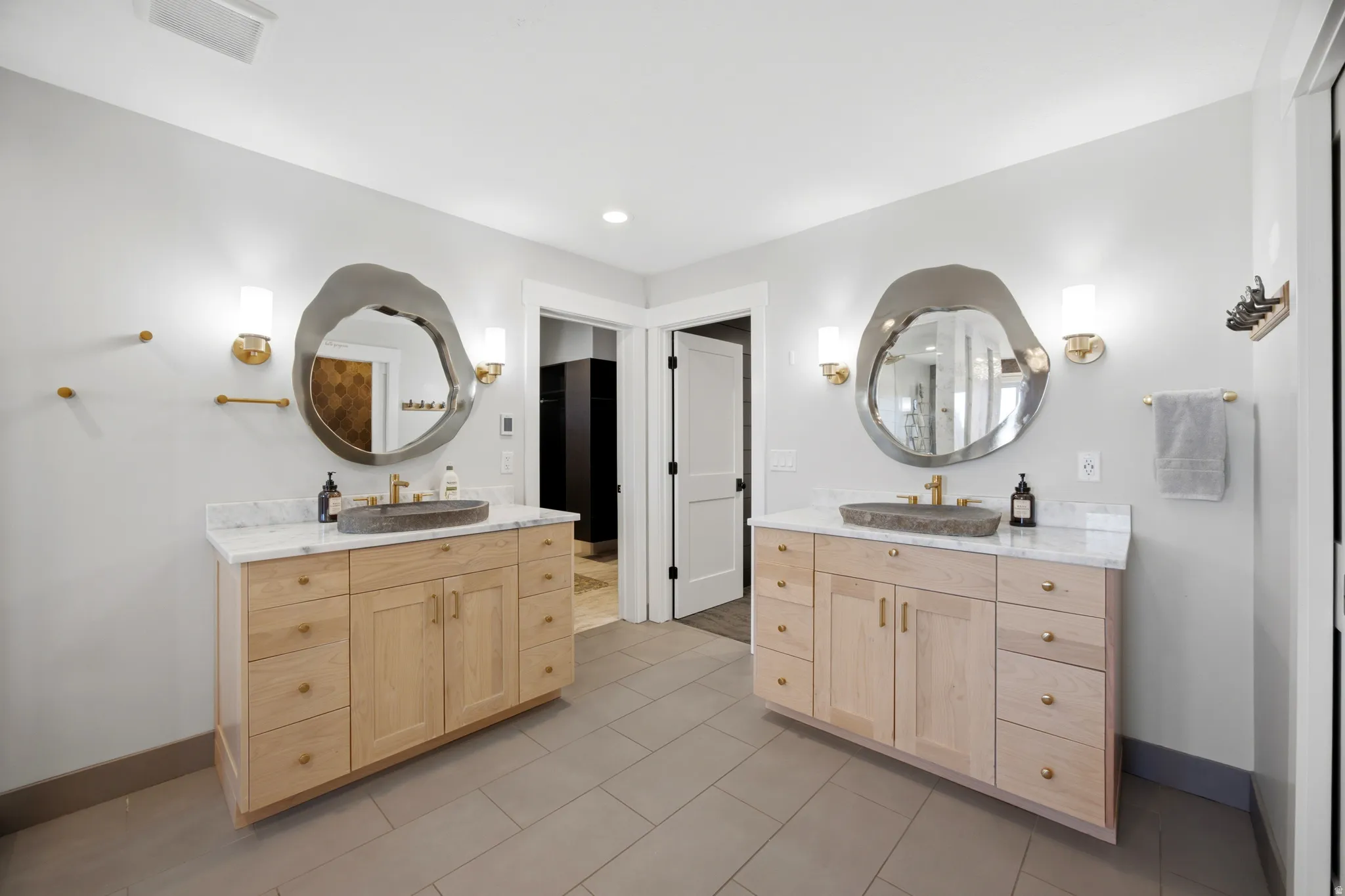 Dual wood-finish vanities with stone vessel sinks, marble countertops, and unique organic-shaped mirrors