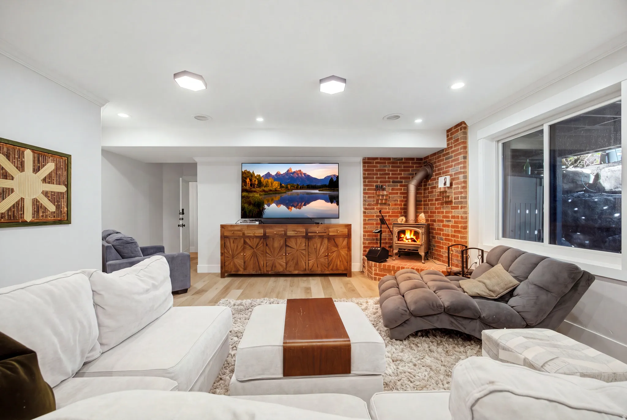 Exposed brick accent wall with a wood-burning stove, recessed lighting, wood-finish flooring, and a large window