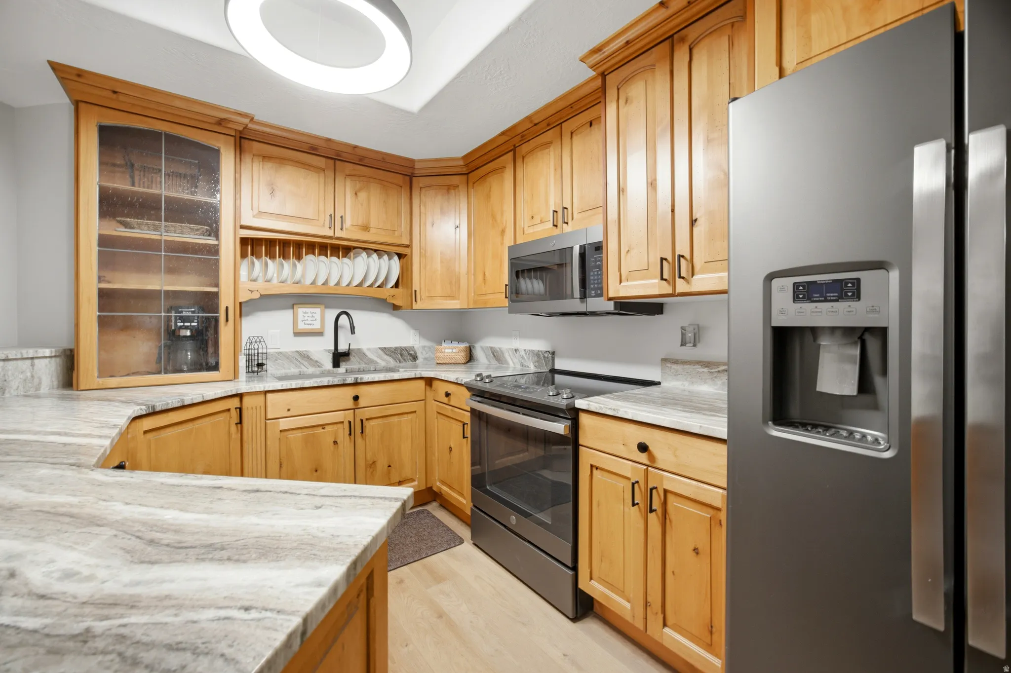 Wood-finish cabinetry with black hardware, stone countertops, stainless steel appliances, and wood-finish flooring