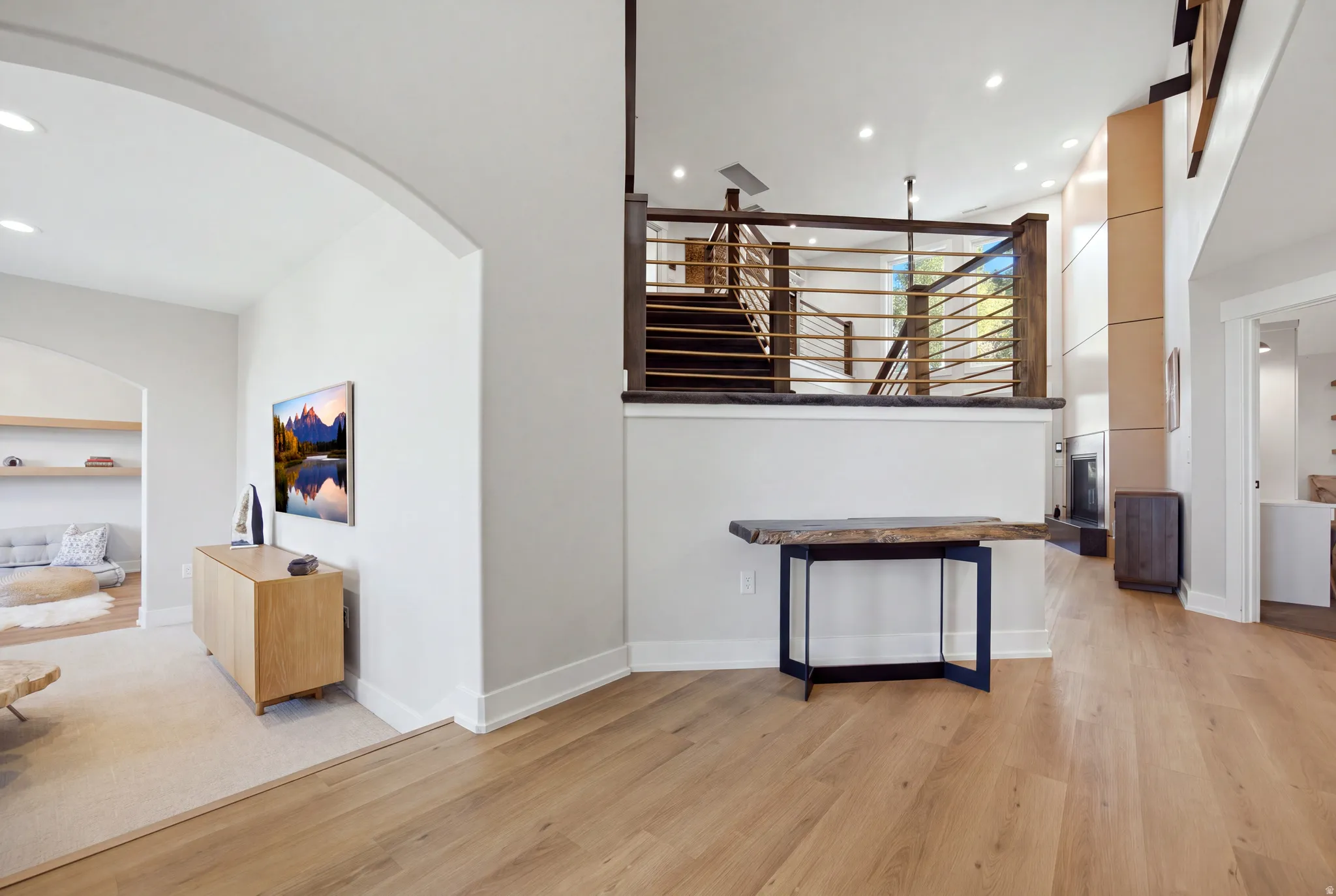 Wood-finish flooring throughout, arched doorway, recessed lighting, modern staircase with metal balusters, and a built-in entertainment wall
