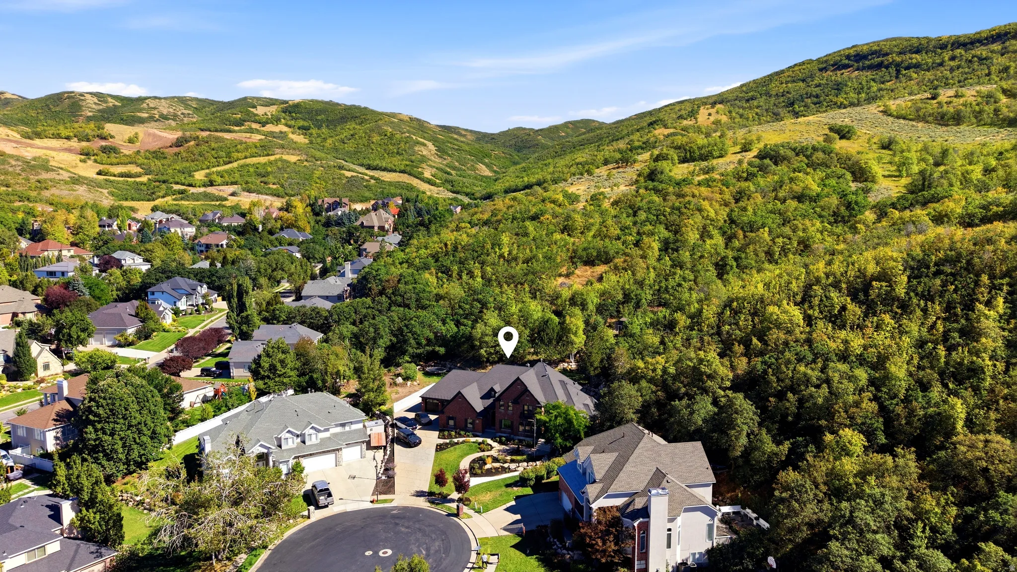 Property situated on a cul-de-sac with a brick exterior and a paved driveway, surrounded by mature trees and natural landscaping