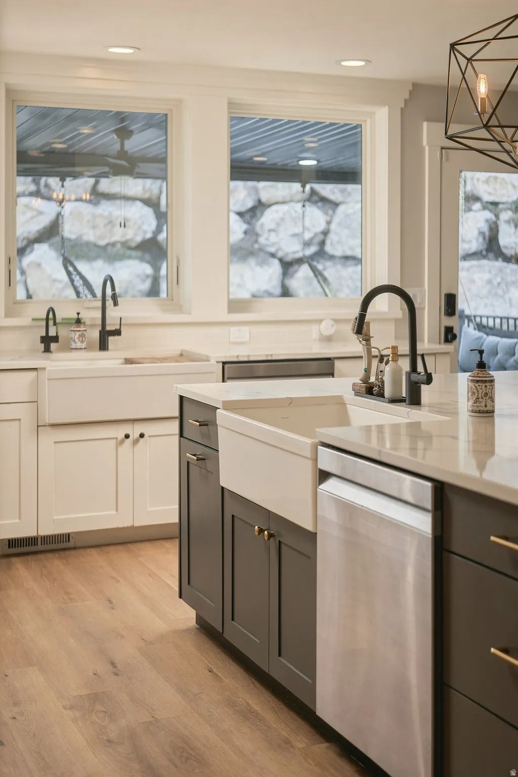 Kitchen featuring wood-finish flooring, two large windows, white and gray cabinetry, a farmhouse sink, and a stainless steel dishwasher