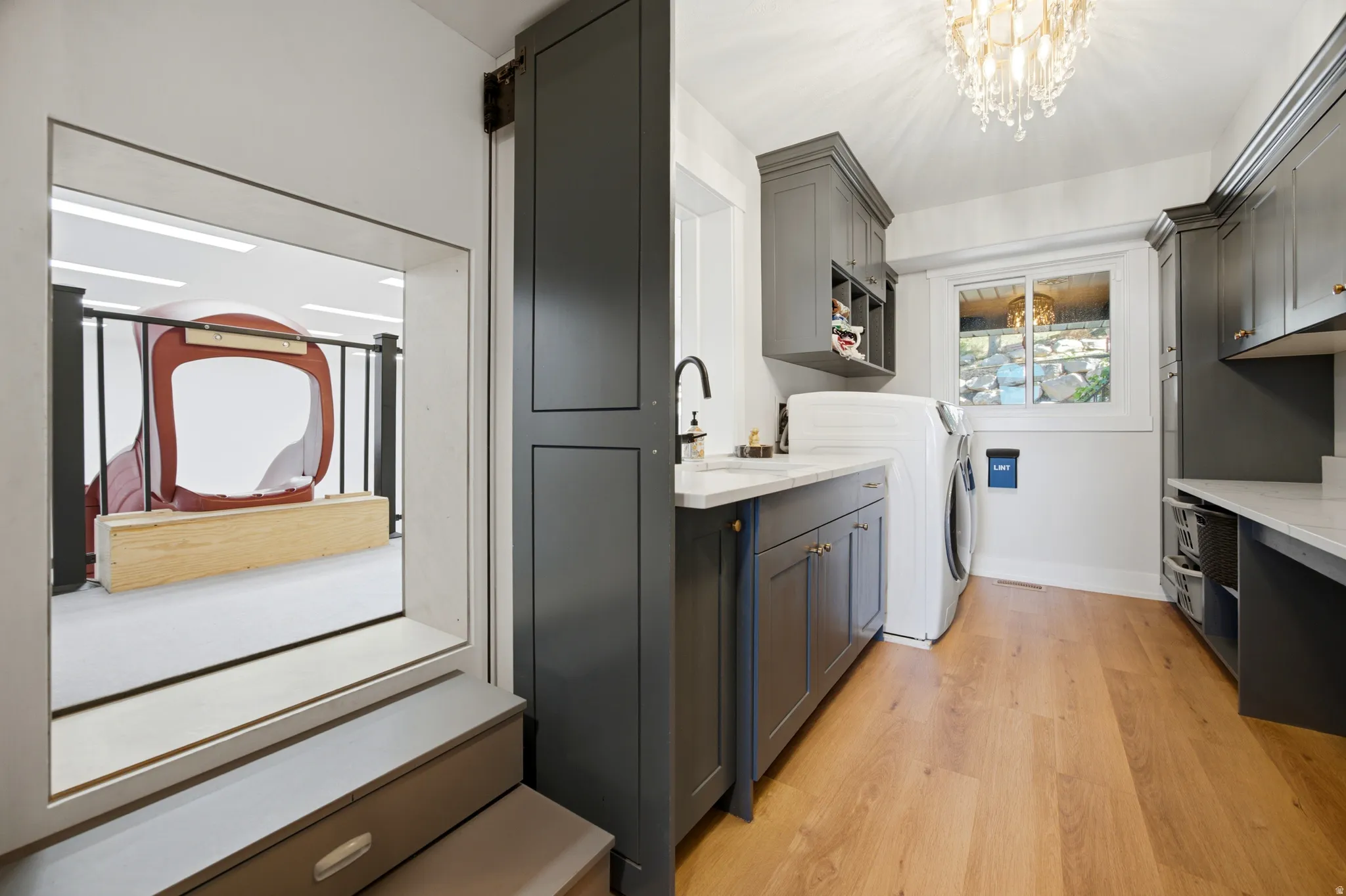 Laundry area featuring wood-finish flooring, shaker-style cabinetry, a built-in countertop, and a double-hung window