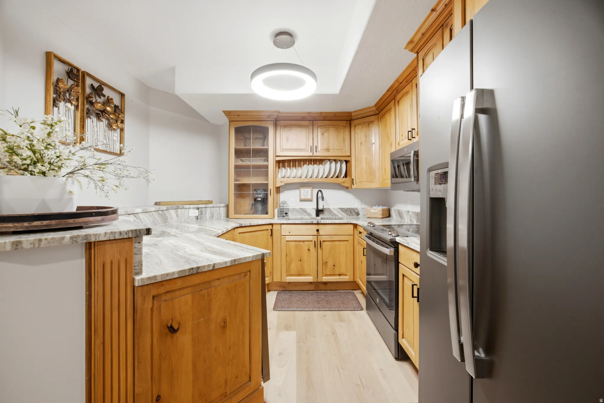 Kitchen featuring light wood cabinetry, light stone countertops, stainless steel appliances, and wood-finish flooring