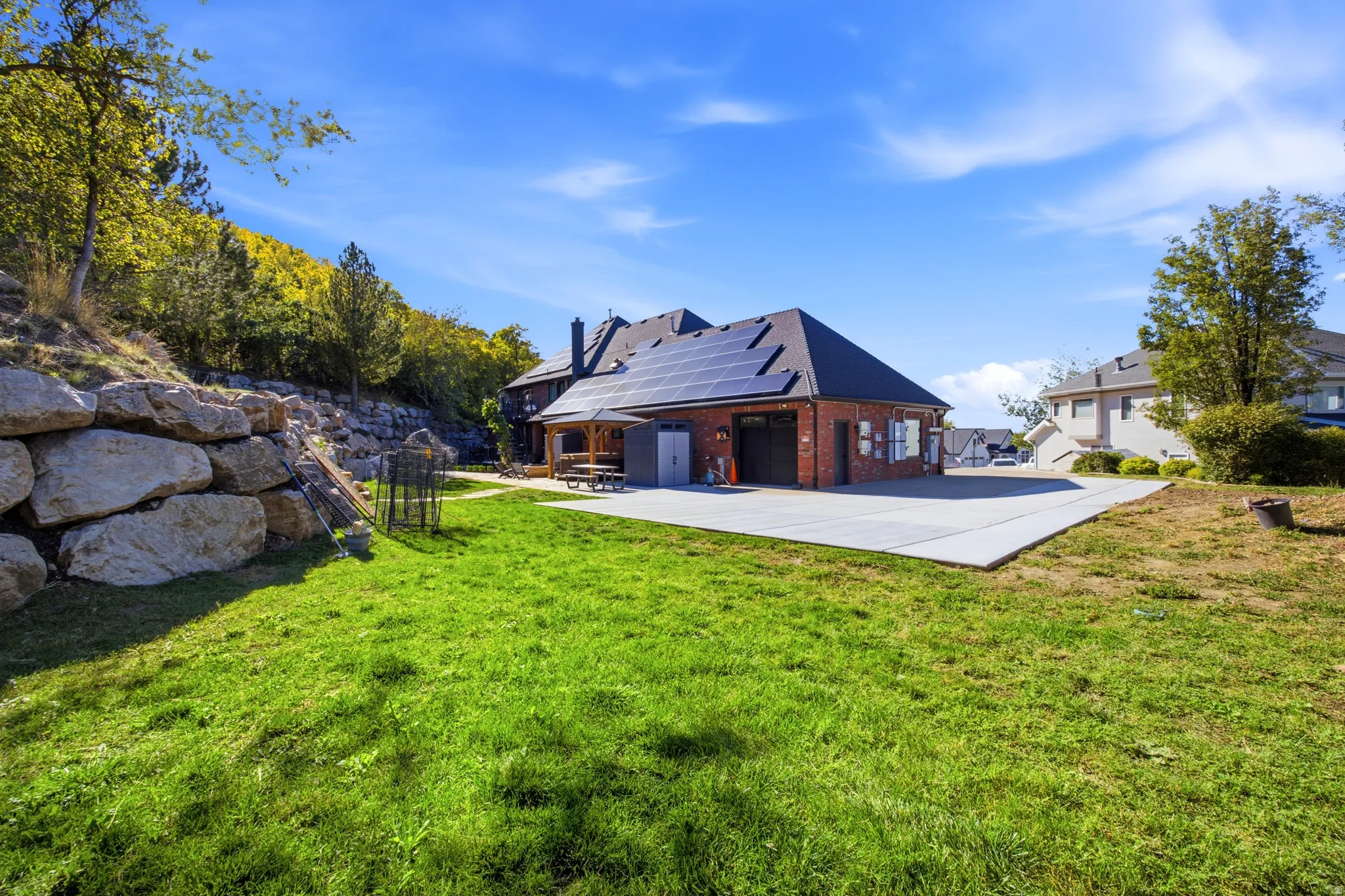 Expansive green lawn, stone retaining wall, large concrete patio, brick exterior, and rooftop solar panels