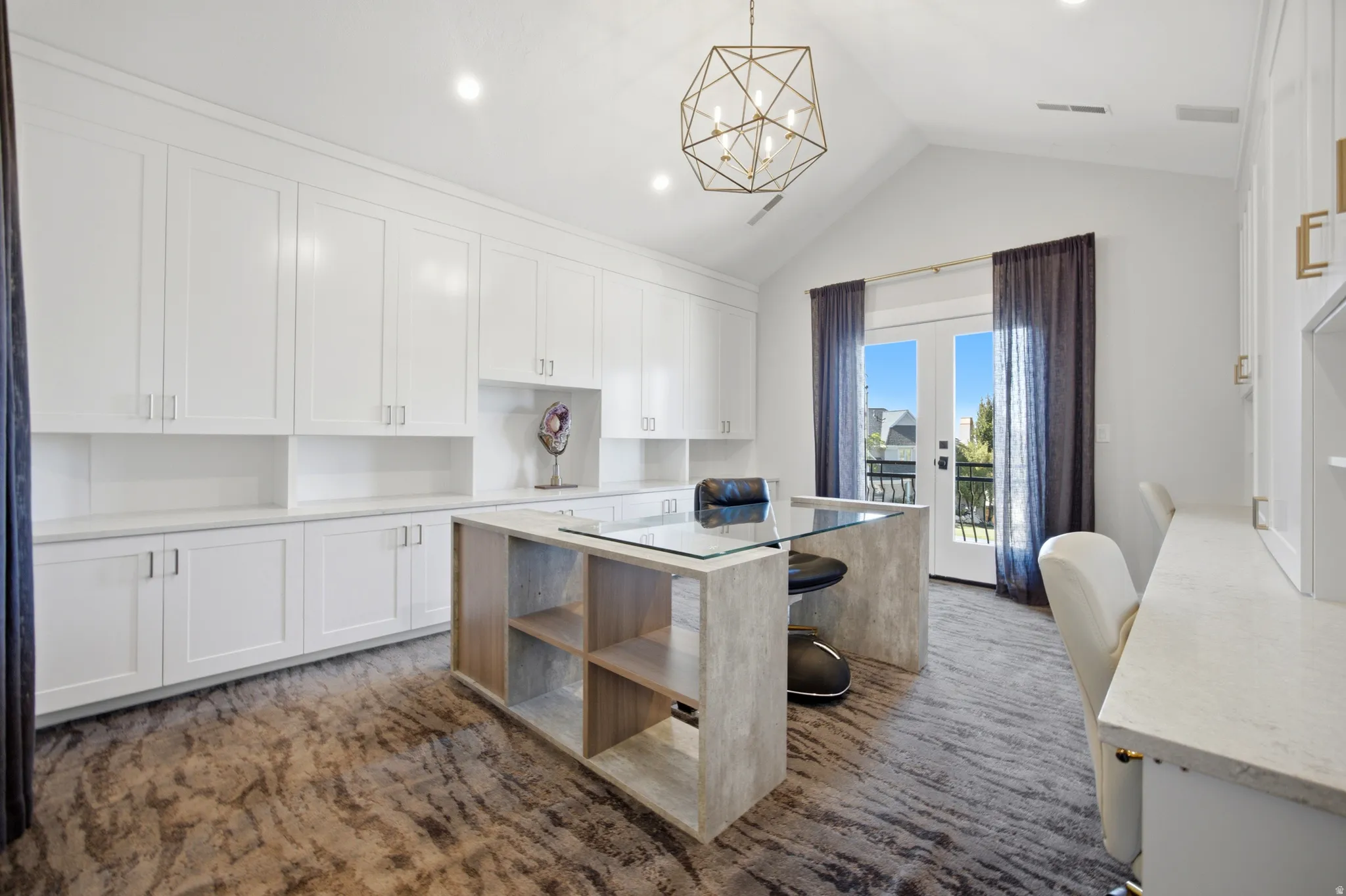 Vaulted ceiling with a geometric chandelier, extensive built-in white cabinetry, light-toned countertop surfaces, French doors with exterior railing, and patterned flooring