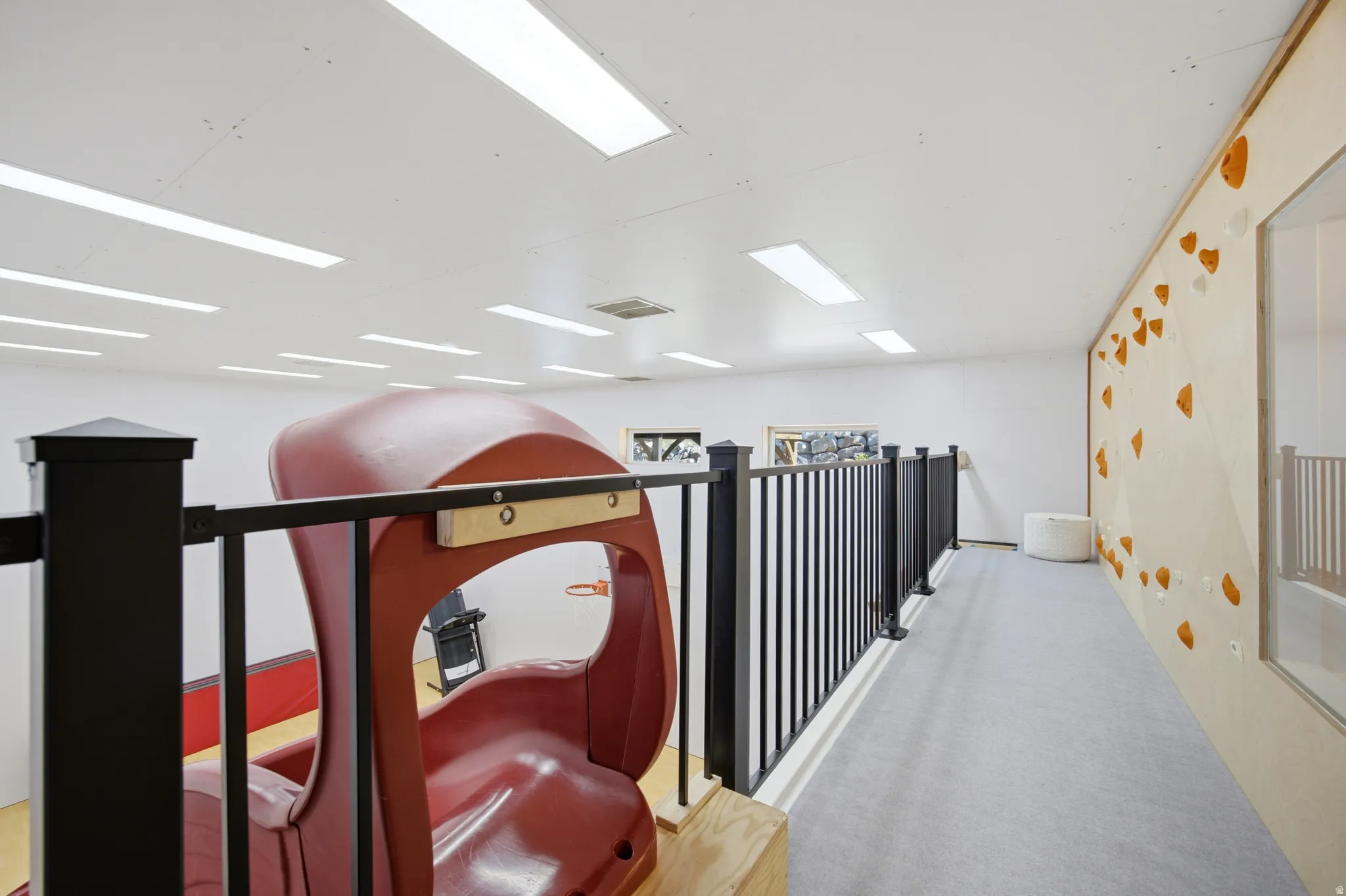 Loft space with black railing, light-colored climbing wall, and recessed lighting