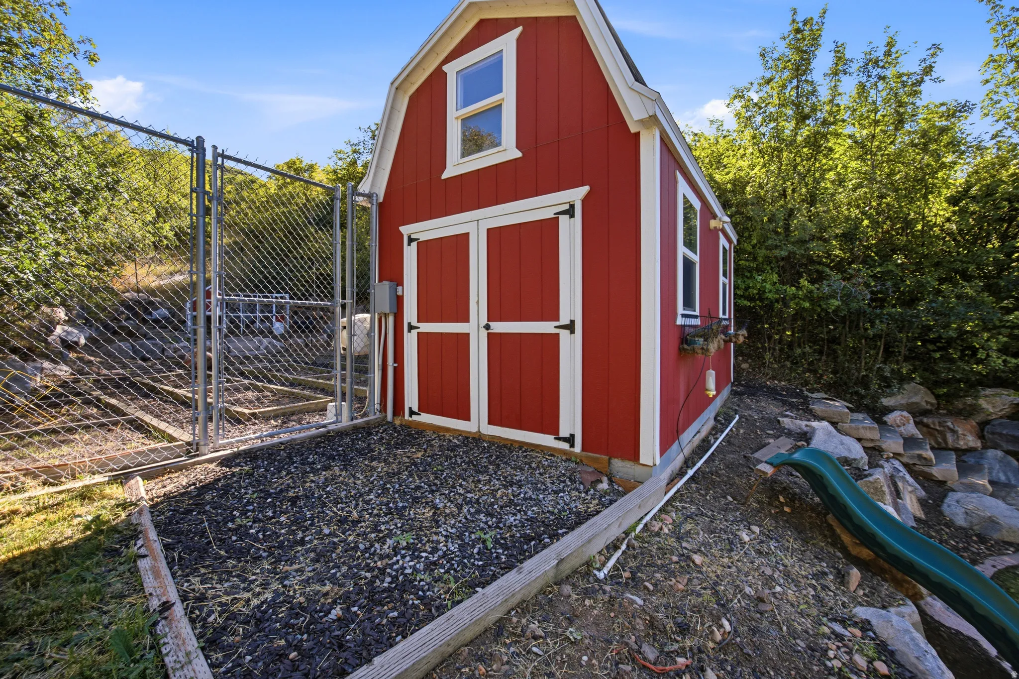 Red gambrel-style shed with white trim, dual doors, and side windows
