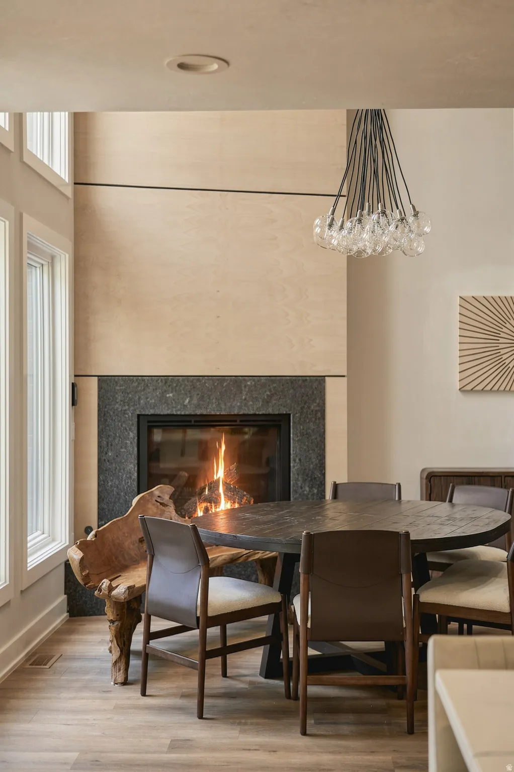 Wood-finish flooring, integrated fireplace with a dark stone surround, wood-paneled wall, and multiple tall windows