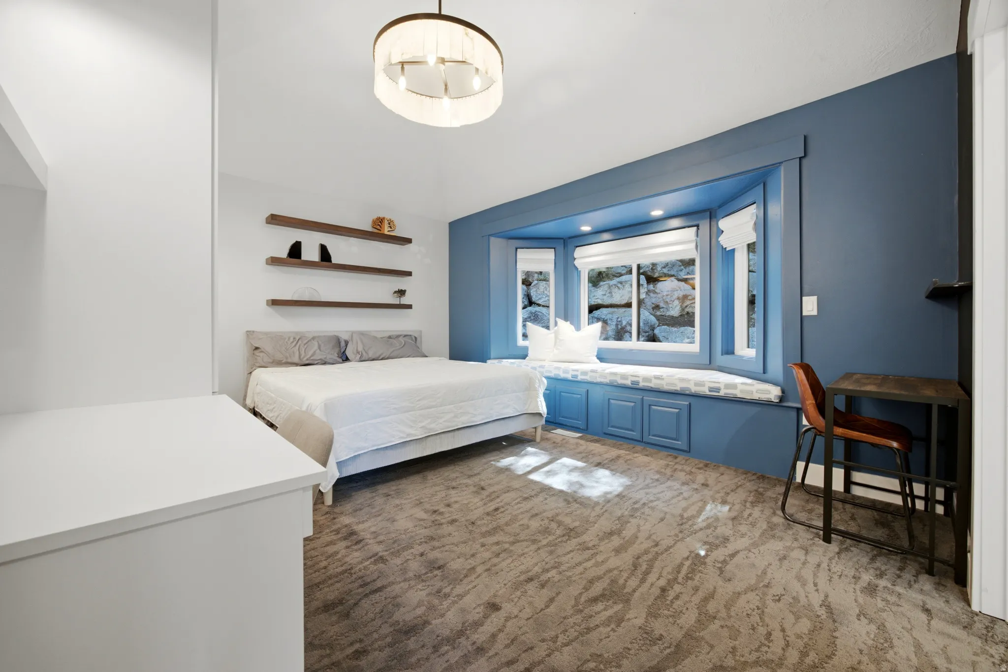 Carpeted interior space featuring a built-in window seat with integrated storage, wood-finish floating shelves, and a contemporary ceiling fixture