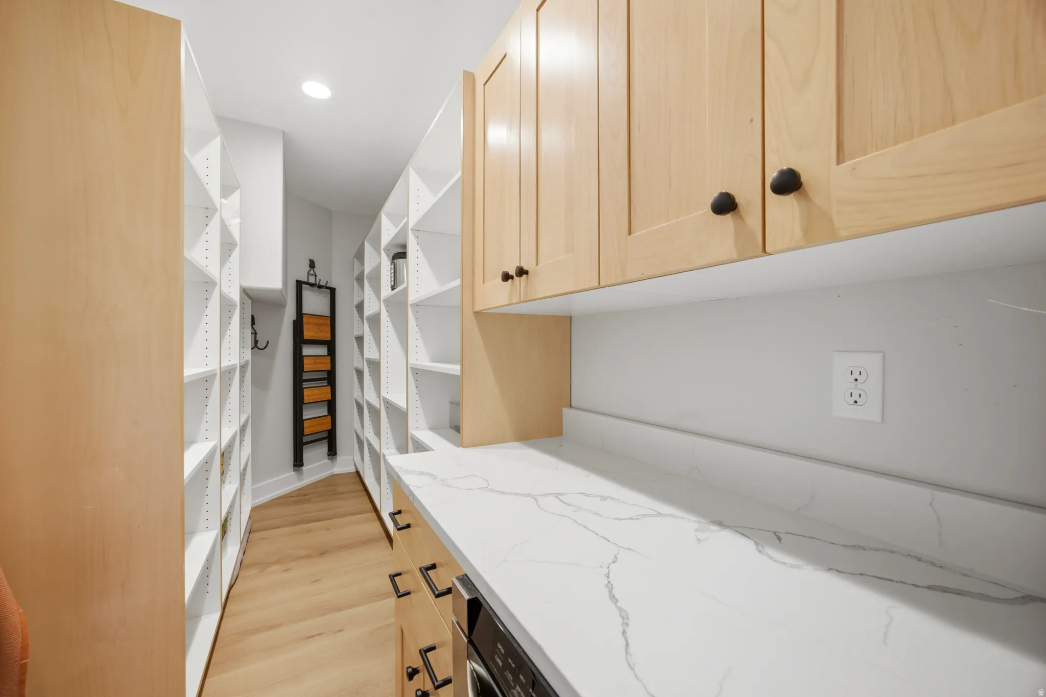 Extensive built-in shelving, wood-finish flooring, light wood cabinetry, white stone-finish countertop, and recessed lighting
