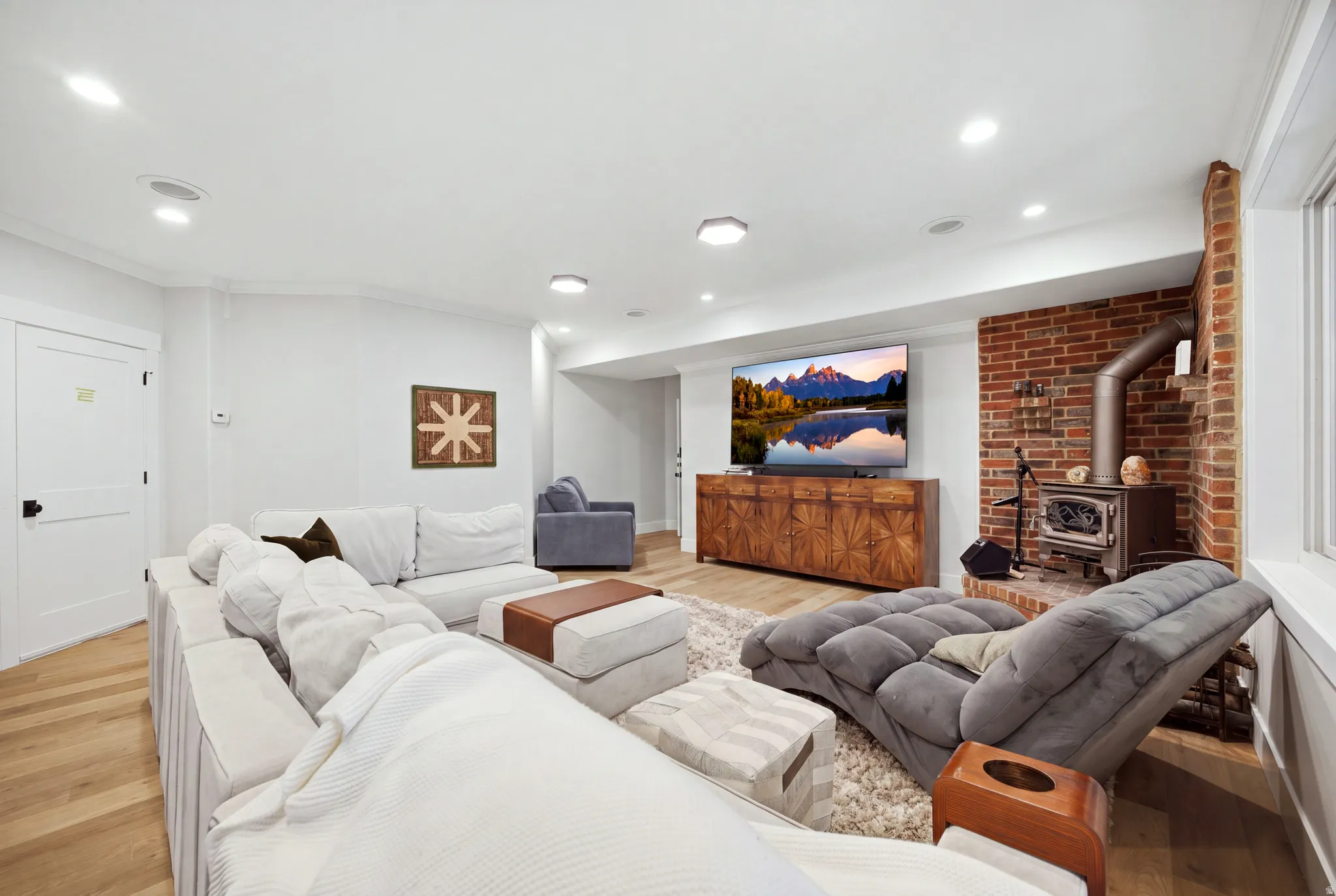Recessed lighting, wood-finish flooring, and a brick accent wall with a built-in wood-burning stove