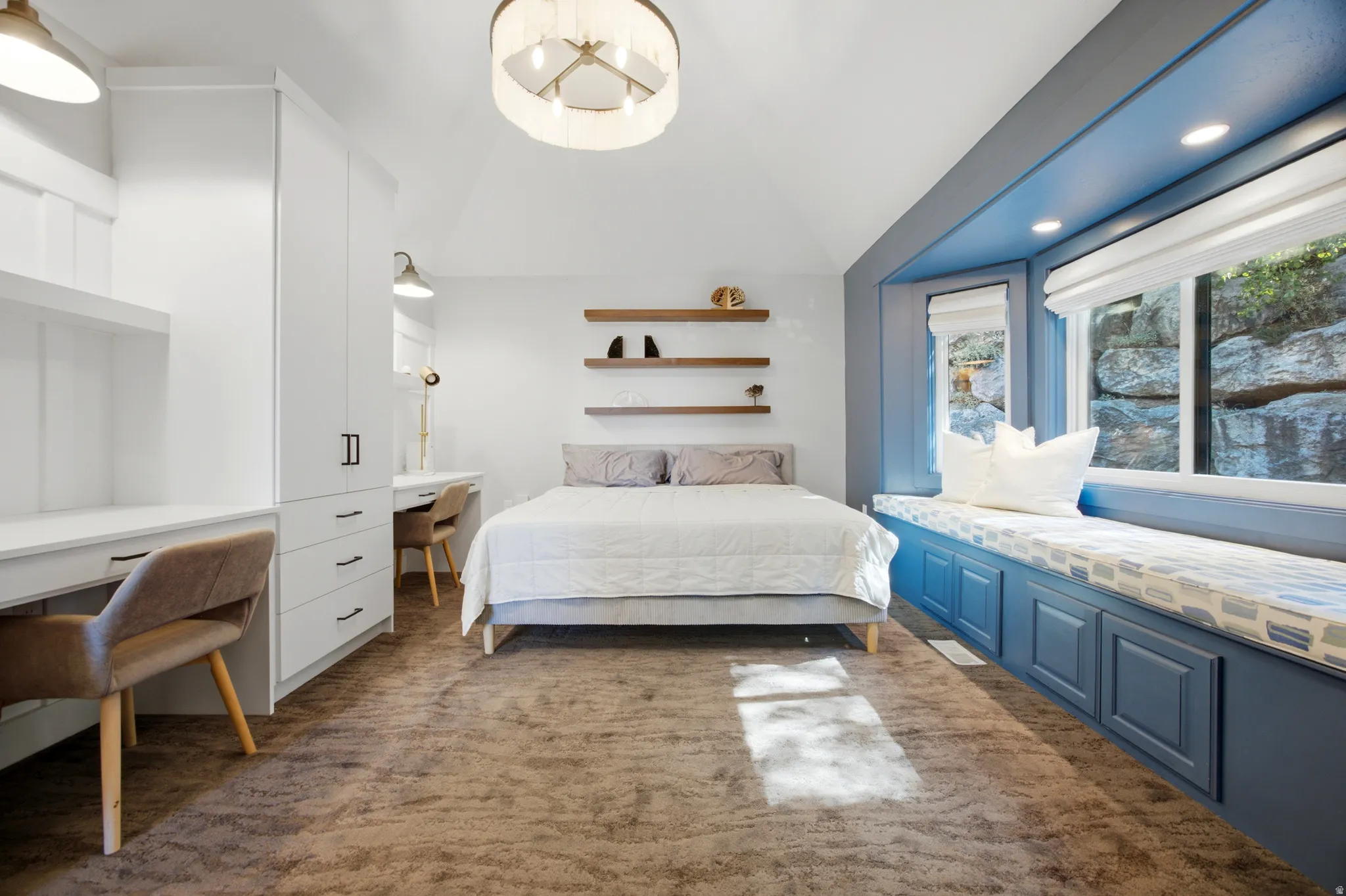 Built-in window seat with integrated storage, custom desks with shelving, recessed lighting, and a vaulted ceiling