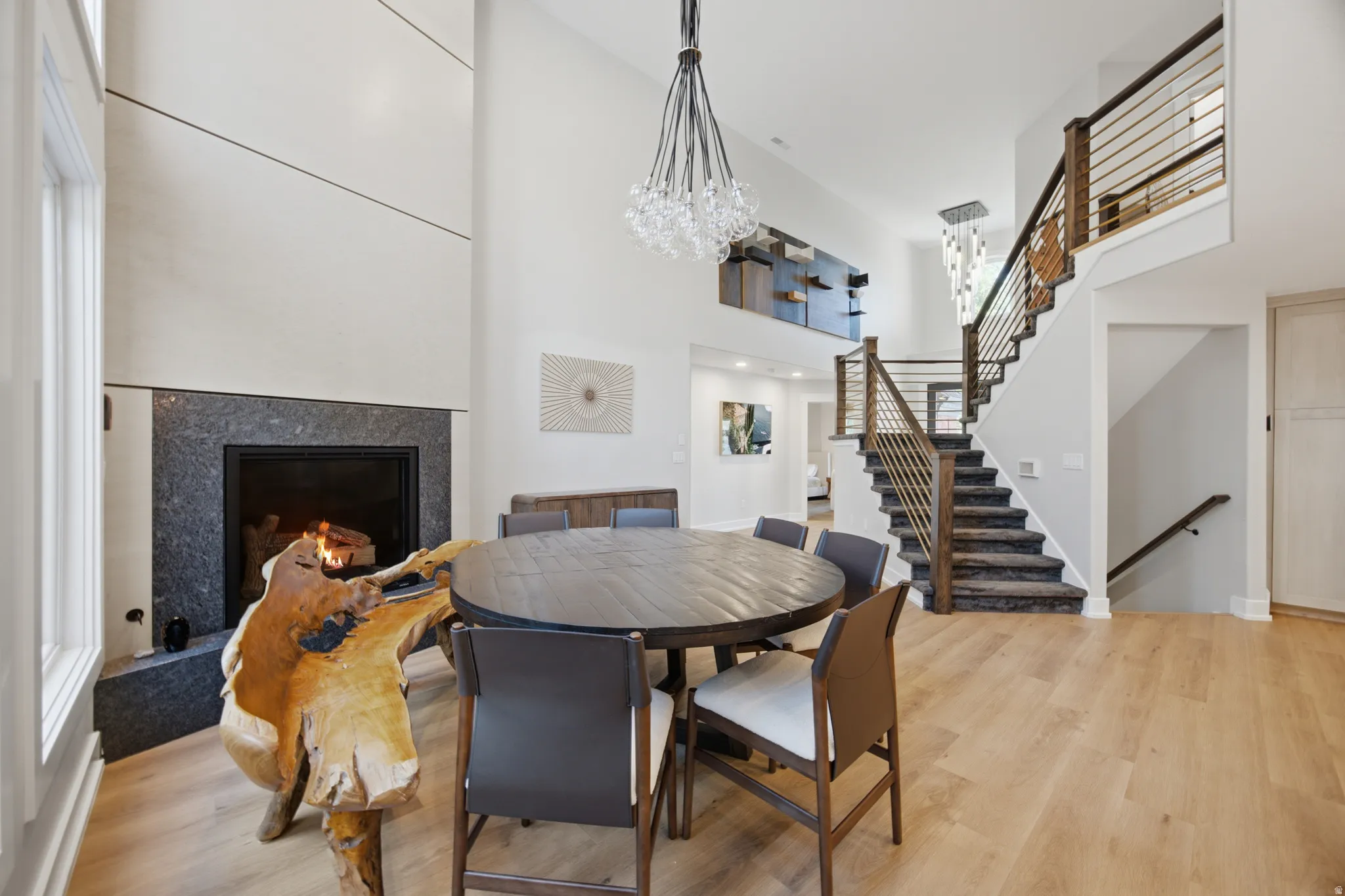 Vaulted ceilings, wood-finish flooring, a contemporary chandelier, a staircase with metal balusters, and a fireplace with a stone surround