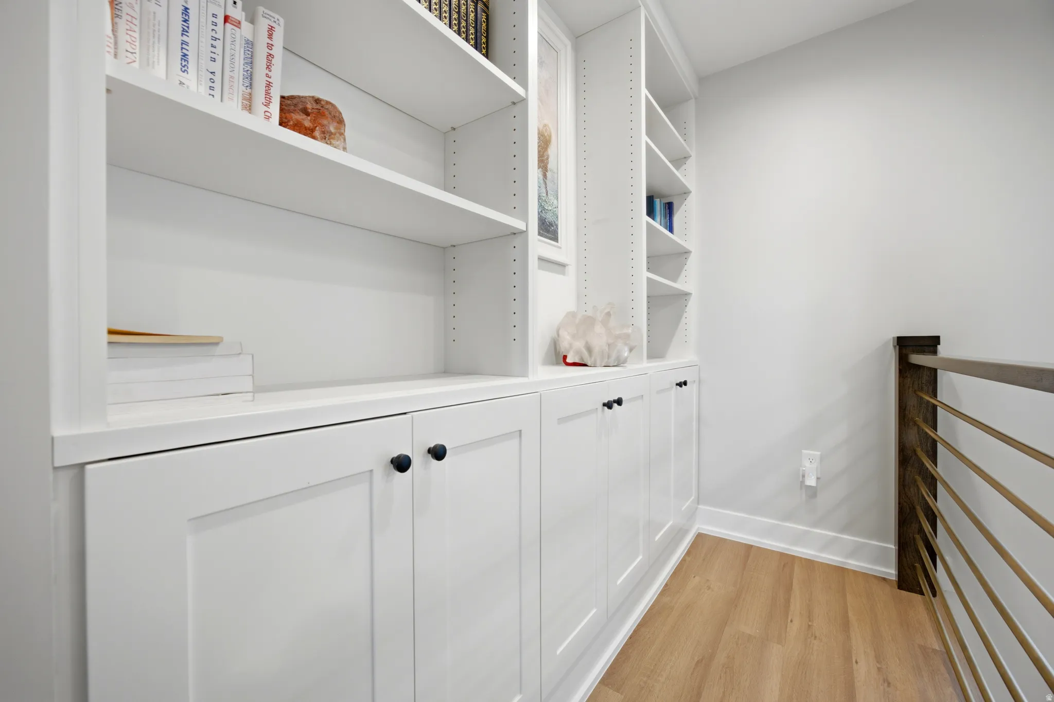 Built-in white cabinetry with black hardware, integrated shelving, wood-finish flooring, and a contemporary metal and wood railing