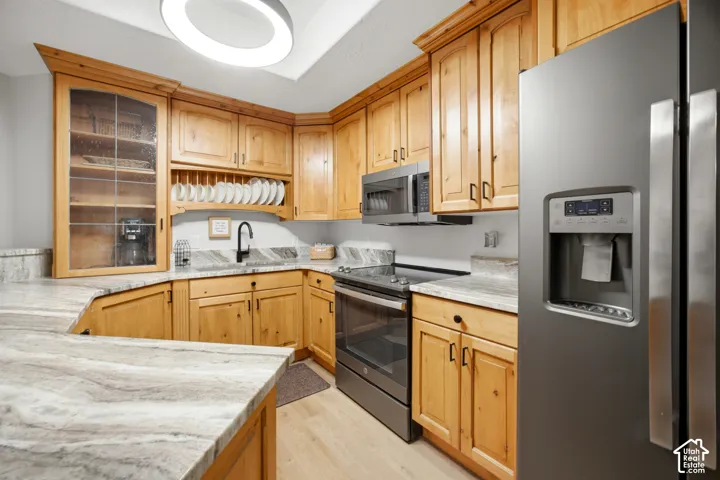 Wood-finish cabinetry with black hardware, stone countertops, stainless steel appliances, and wood-finish flooring