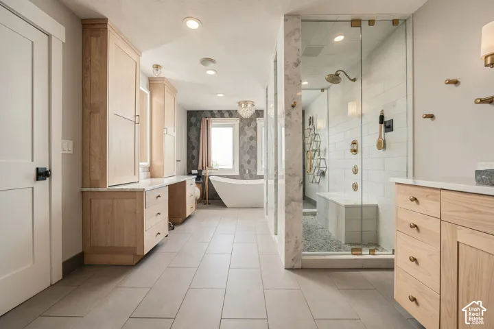 Dual light wood-finish vanities with stone countertops, a freestanding soaking tub, a spacious glass-enclosed shower with a built-in bench, and large format tile flooring