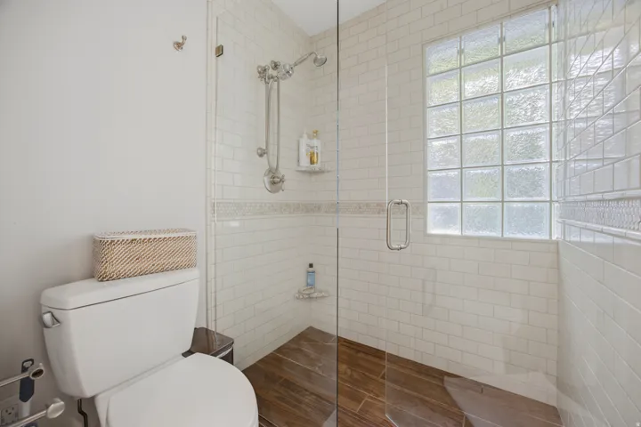 Glass-enclosed shower with subway tile walls, a decorative tile accent, and a glass block window
