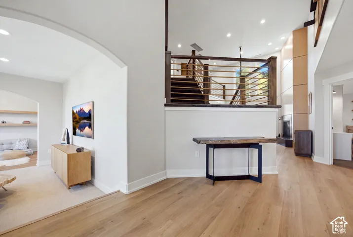 Wood-finish flooring throughout, arched doorway, recessed lighting, modern staircase with metal balusters, and a built-in entertainment wall