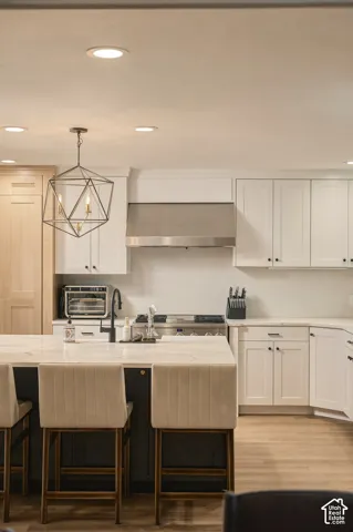 White shaker cabinetry, stainless steel range hood, stone countertops, geometric pendant lighting, and wood-finish flooring