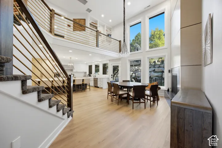 Open-concept living space with light wood-finish flooring, a two-story ceiling, and a prominent staircase with cable railings