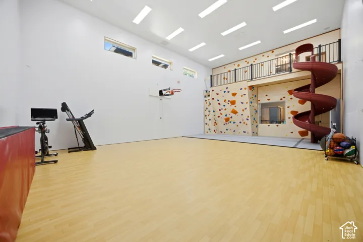 Expansive recreational space featuring wood-finish flooring, a built-in climbing wall, an indoor spiral slide, and a basketball hoop